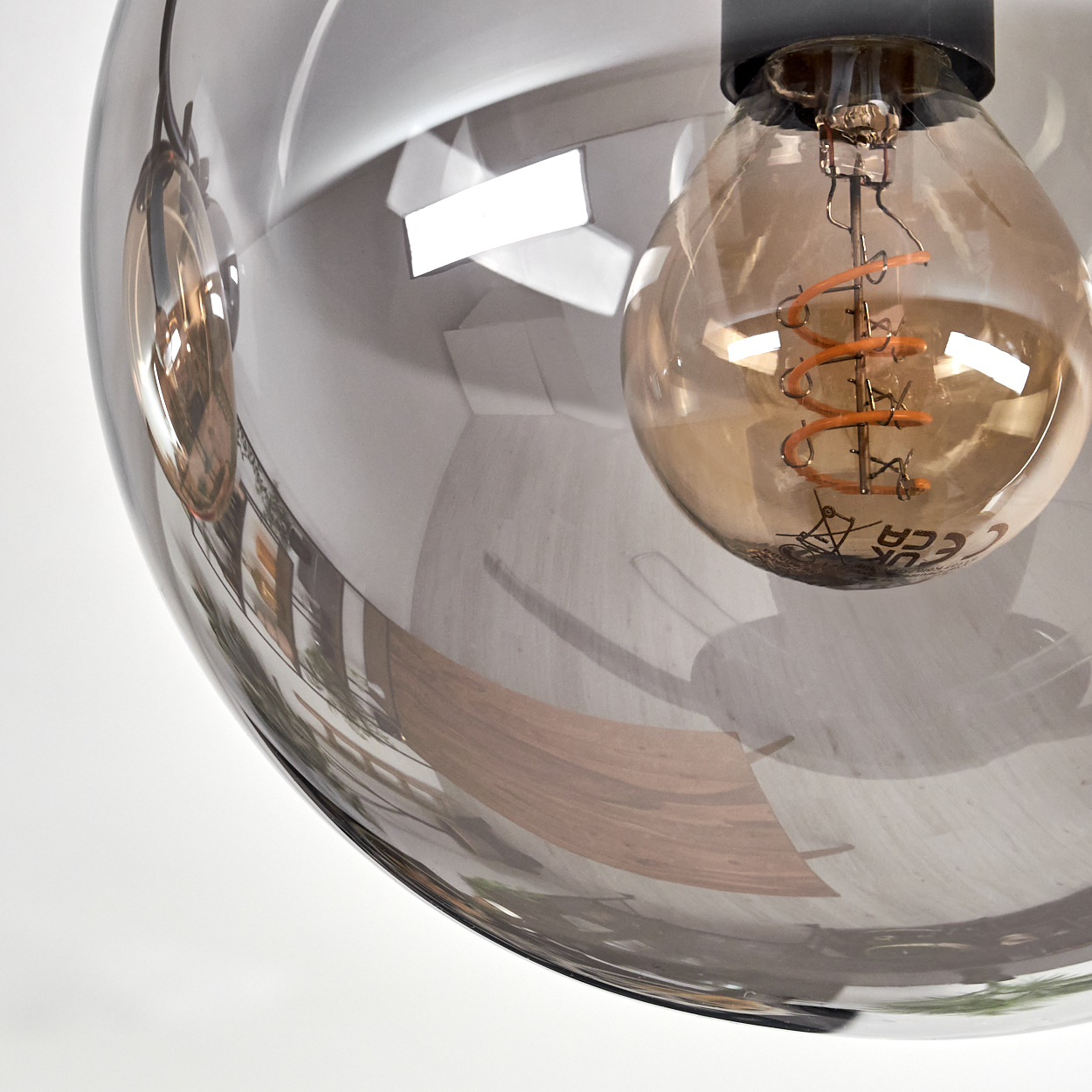 Nahaufnahme einer Glasleuchte mit Glühbirne. Das Glas reflektiert, wodurch der Raum sichtbar wird. Die Glühbirne leuchtet.