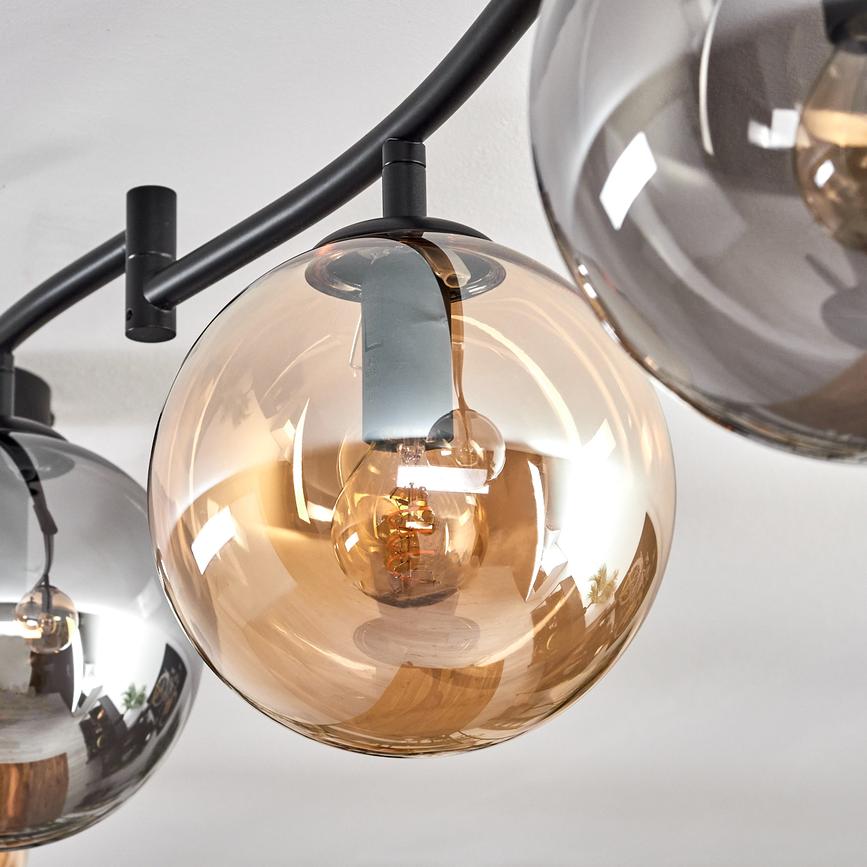 Eine moderne Leuchte mit drei Glasschirmen, zwei bernsteinfarbenen und einem grauen, mit freiliegenden Glühbirnen. Schwarze Metallarme halten sie.