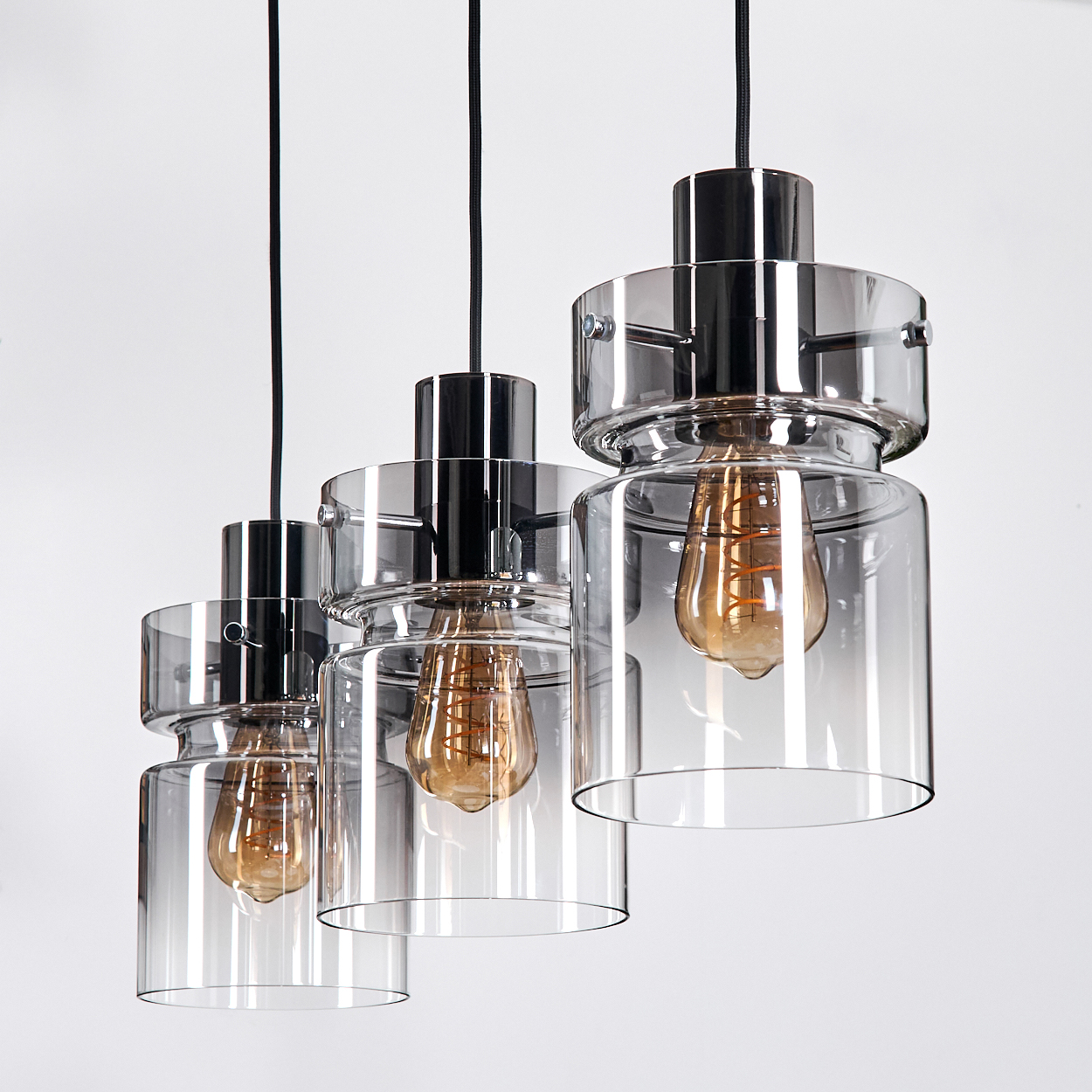 Drei Pendelleuchten mit Glasschirmen und Edison-Glühbirnen hängen vor weißem Hintergrund.