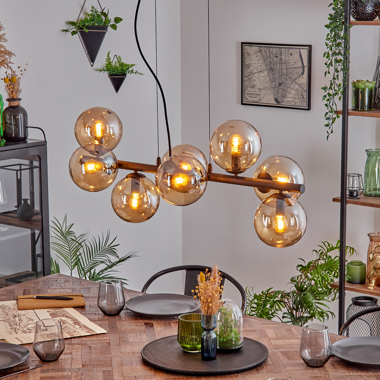 Ein Esszimmer mit Holztisch, modernem Kronleuchter mit Kugellichtern und Pflanzen.