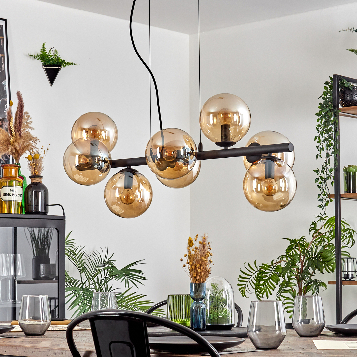 Ein Esszimmer zeigt einen modernen Kronleuchter, Tischgedeck, Pflanzen und Vasen. Der Kronleuchter hat bernsteinfarbene Glaskugeln.