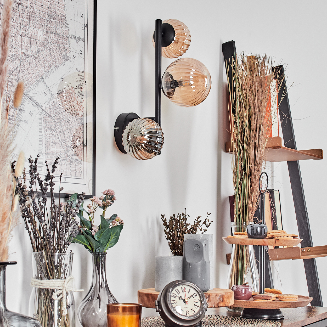 Ein Raum mit Dekoration. Eine Wandlampe, eine Karte, Blumen, eine Uhr und ein Leiterregal sind ausgestellt. Die Farben sind neutral mit warmen Akzenten.