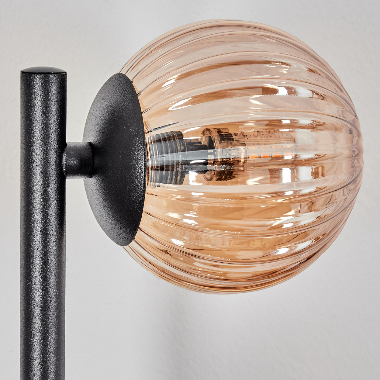 Nahaufnahme einer Lampe. Sie hat einen schwarzen Metallsockel und einen braunen, geriffelten Glaskolben. Der Hintergrund ist weiß.