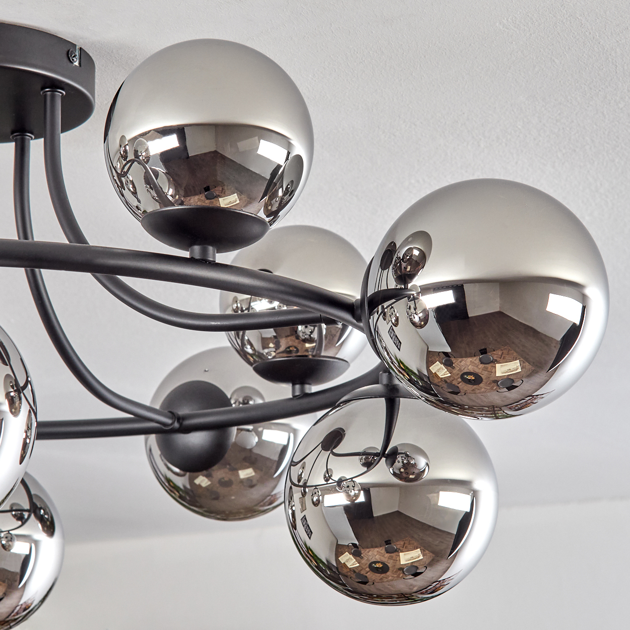 Nahaufnahme eines modernen Kronleuchters mit mehreren glänzenden, reflektierenden Kugeln. Schwarzer Metallrahmen. Weißer Hintergrund.