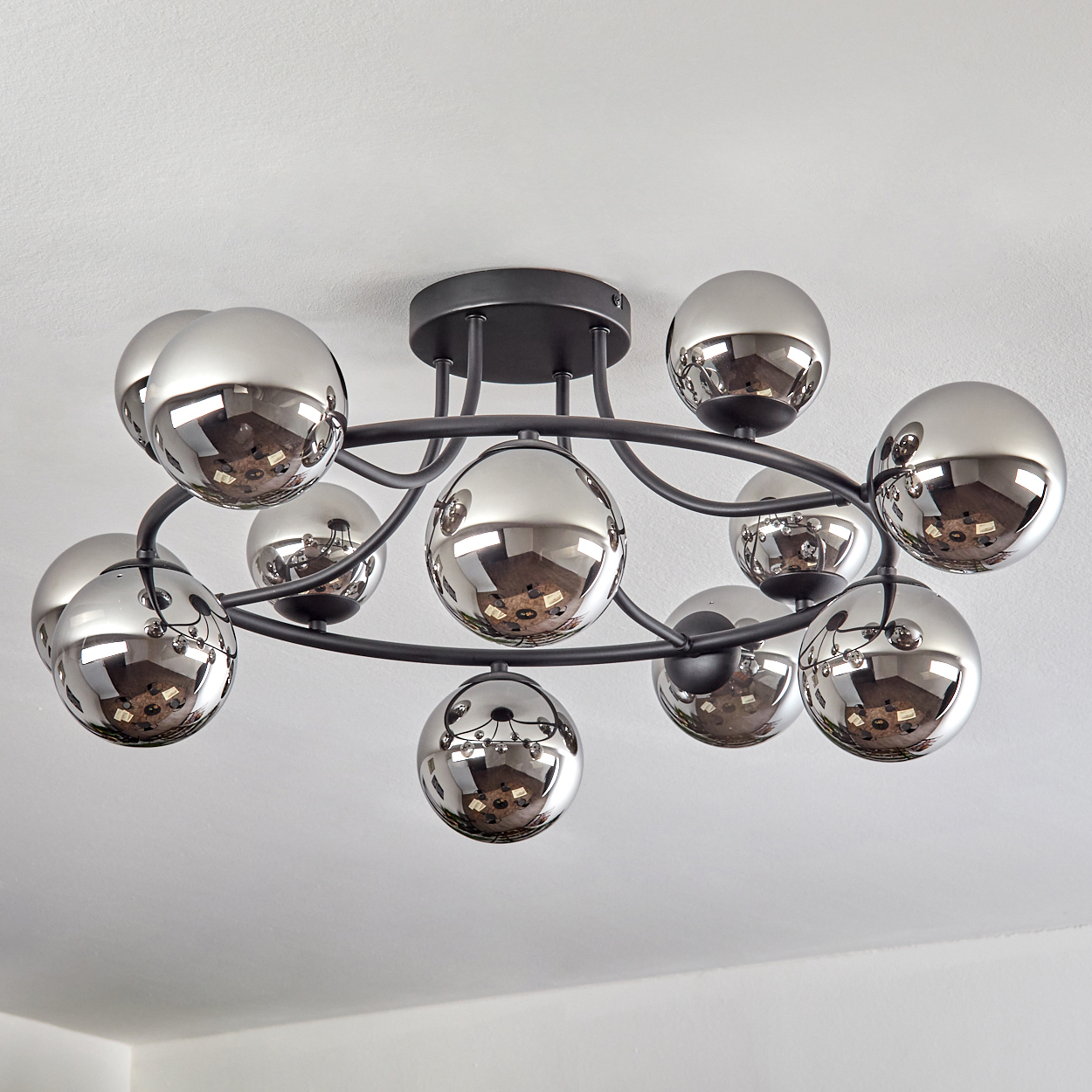 Eine moderne Deckenleuchte mit mehreren Chromkugeln. Die Kugeln reflektieren den Raum. Die Leuchte ist schwarz und an einer weißen Decke montiert.