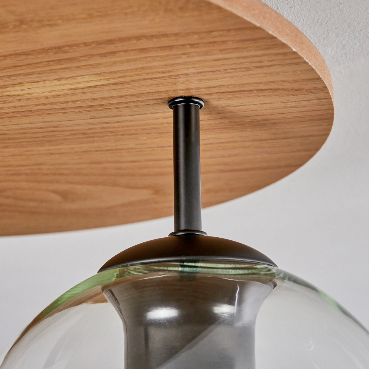 Nahaufnahme einer modernen Leuchte. Sie hat eine Deckenhalterung aus Holz, eine schwarze Stange und einen Glasschirm.