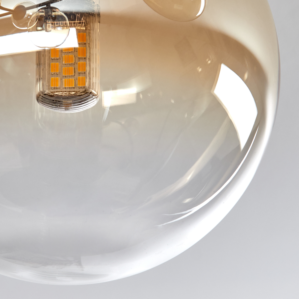 Nahaufnahme einer Leuchte. Eine klare Glaskugel umgibt ein orangefarbenes LED-Licht. Der Hintergrund ist weiß und unscharf.
