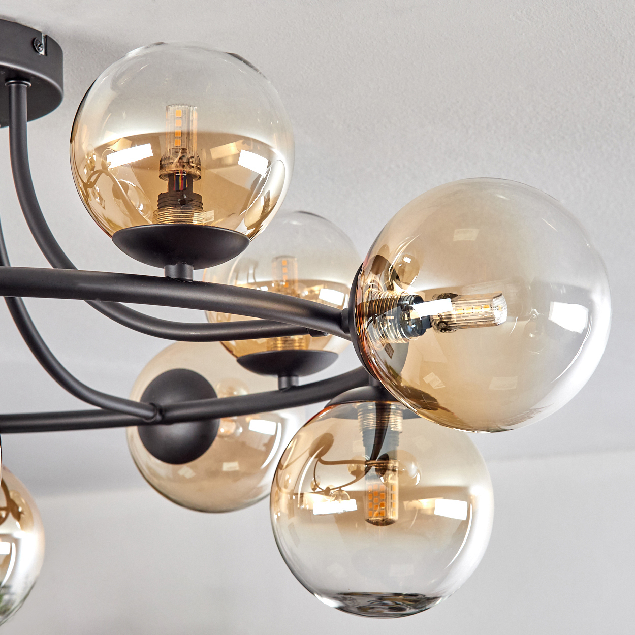Eine moderne Deckenlampe mit mehreren kugelförmigen Glasschirmen in Bernsteinfarbe, montiert auf schwarzen Metallarmen, vor einer weißen Decke.