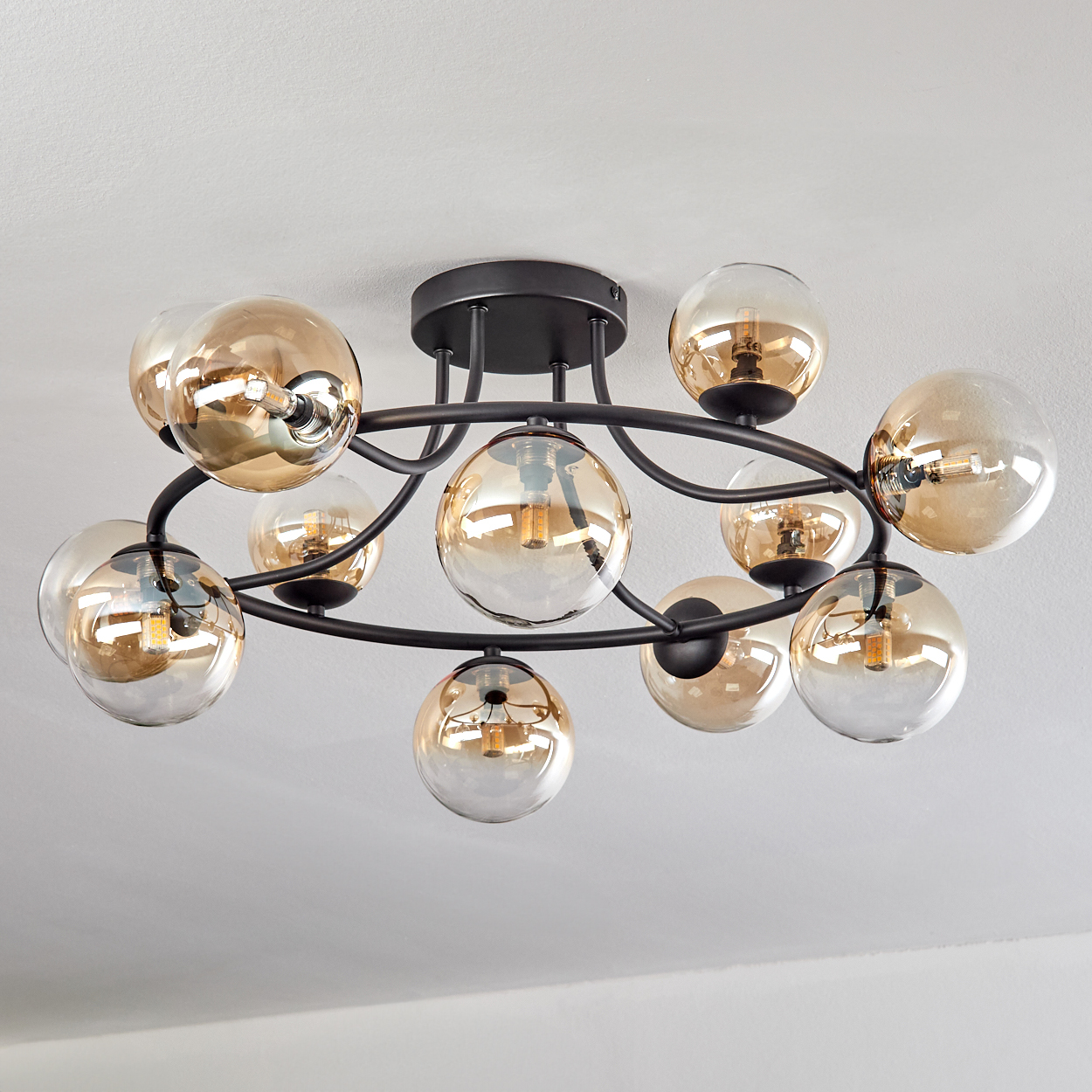 Eine moderne Deckenleuchte mit zehn bernsteinfarbenen Glaskugeln an einem schwarzen Metallrahmen vor weißer Decke.