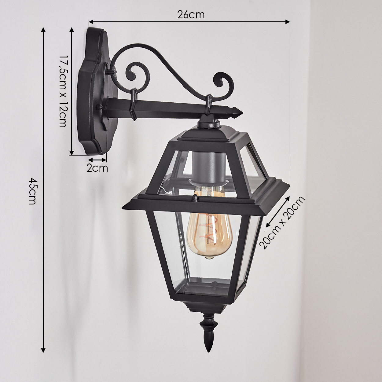 Eine schwarze Außenwandleuchte ist an einer weißen Wand befestigt. Die Lampe hat ein dekoratives Design und eine Vintage-Glühbirne.