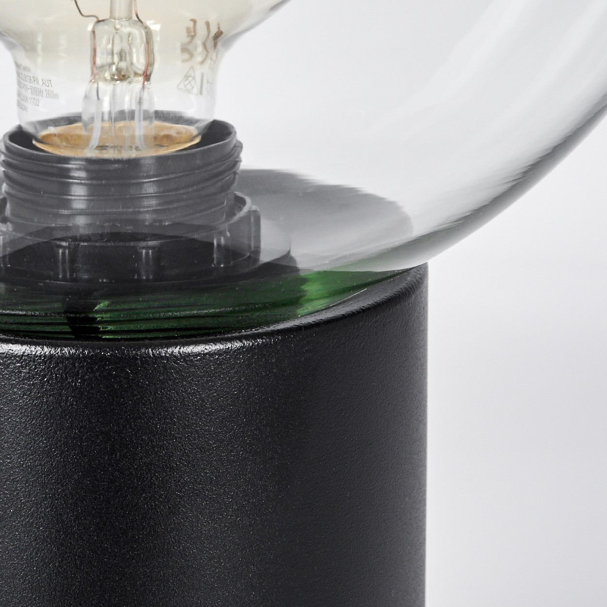 Nahaufnahme einer Lampe. Ein schwarzer Sockel trägt einen Glasschirm. Die Glühbirne ist sichtbar. Grünes Glas ist sichtbar.