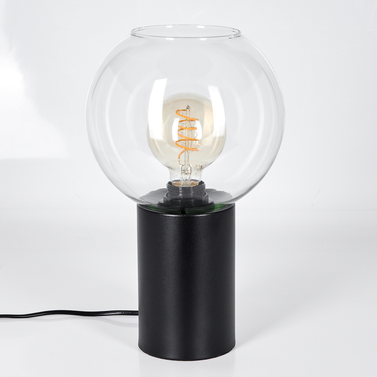 Eine moderne Lampe mit schwarzem zylindrischen Sockel, einer klaren Glaskugel und einer sichtbaren Glühbirne.