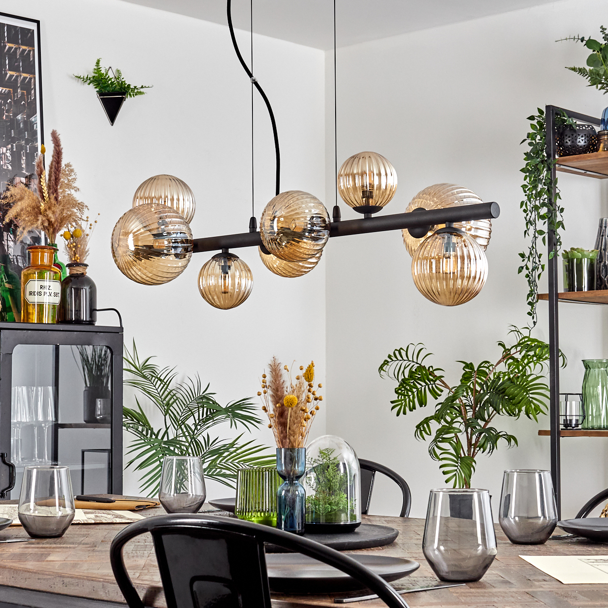 Ein Esszimmer mit Holztisch, schwarzen Stühlen und einer schwarzen Leuchte mit runden Glasschirmen.