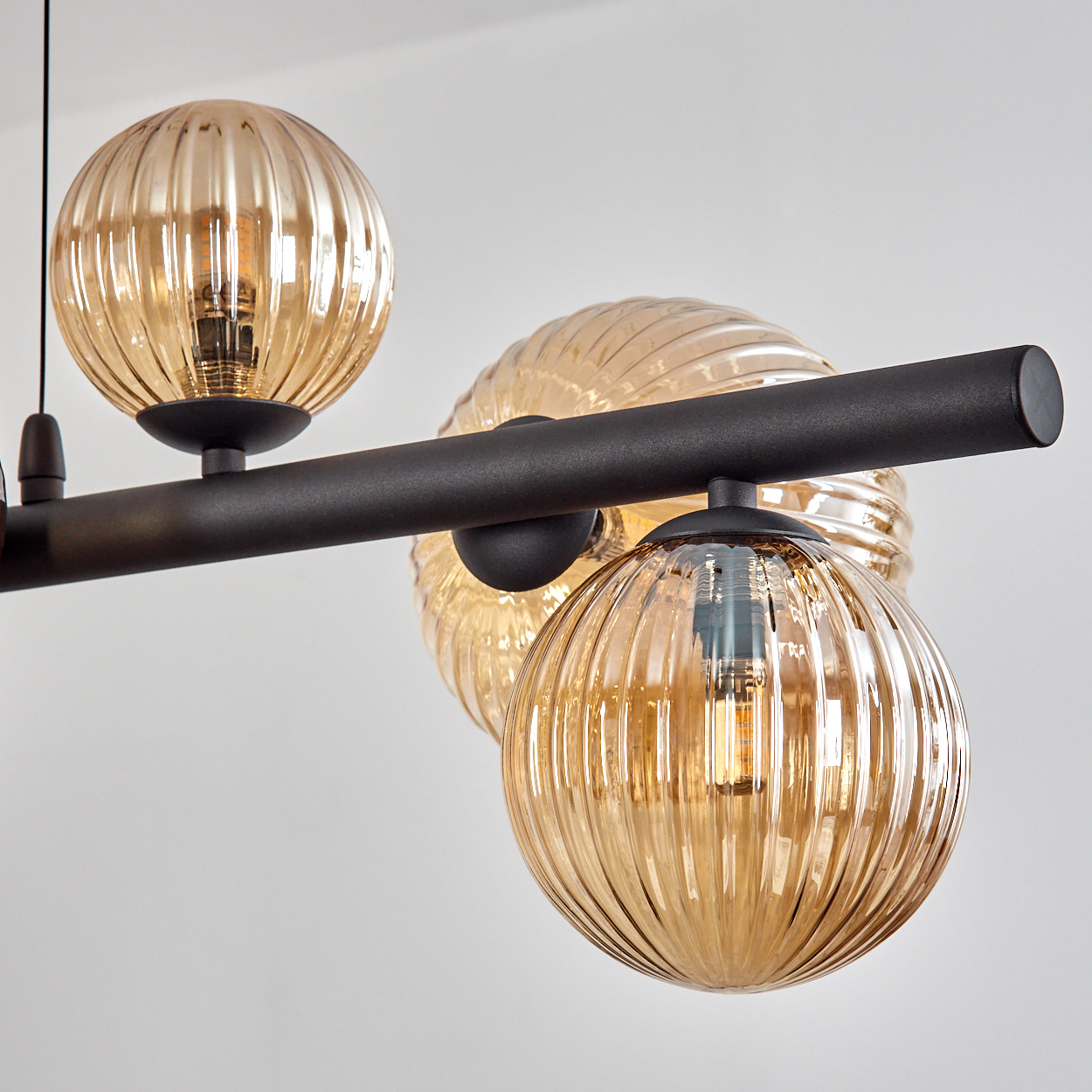 Eine moderne Deckenleuchte mit drei Glaskugeln. Die Kugeln sind bernsteinfarben und gerippt und hängen an einem schwarzen Metallrahmen auf weißem Hintergrund.