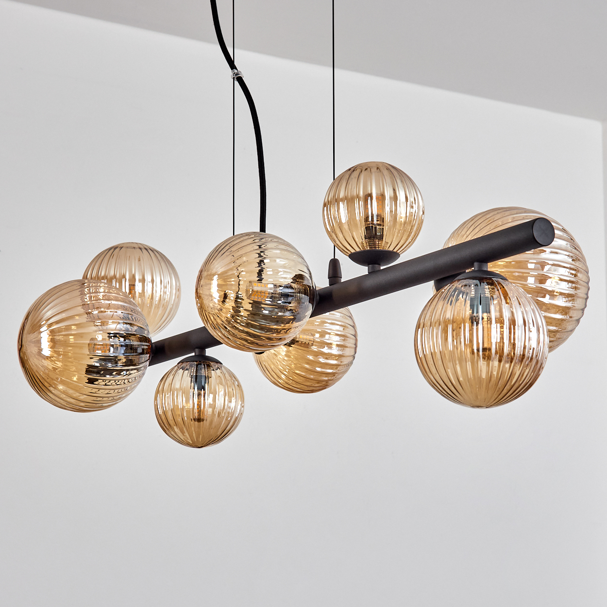 Ein moderner Kronleuchter mit acht gerippten, bernsteinfarbenen Glaskugeln. Er ist an einer schwarzen Metallstange befestigt, die von der Decke hängt.