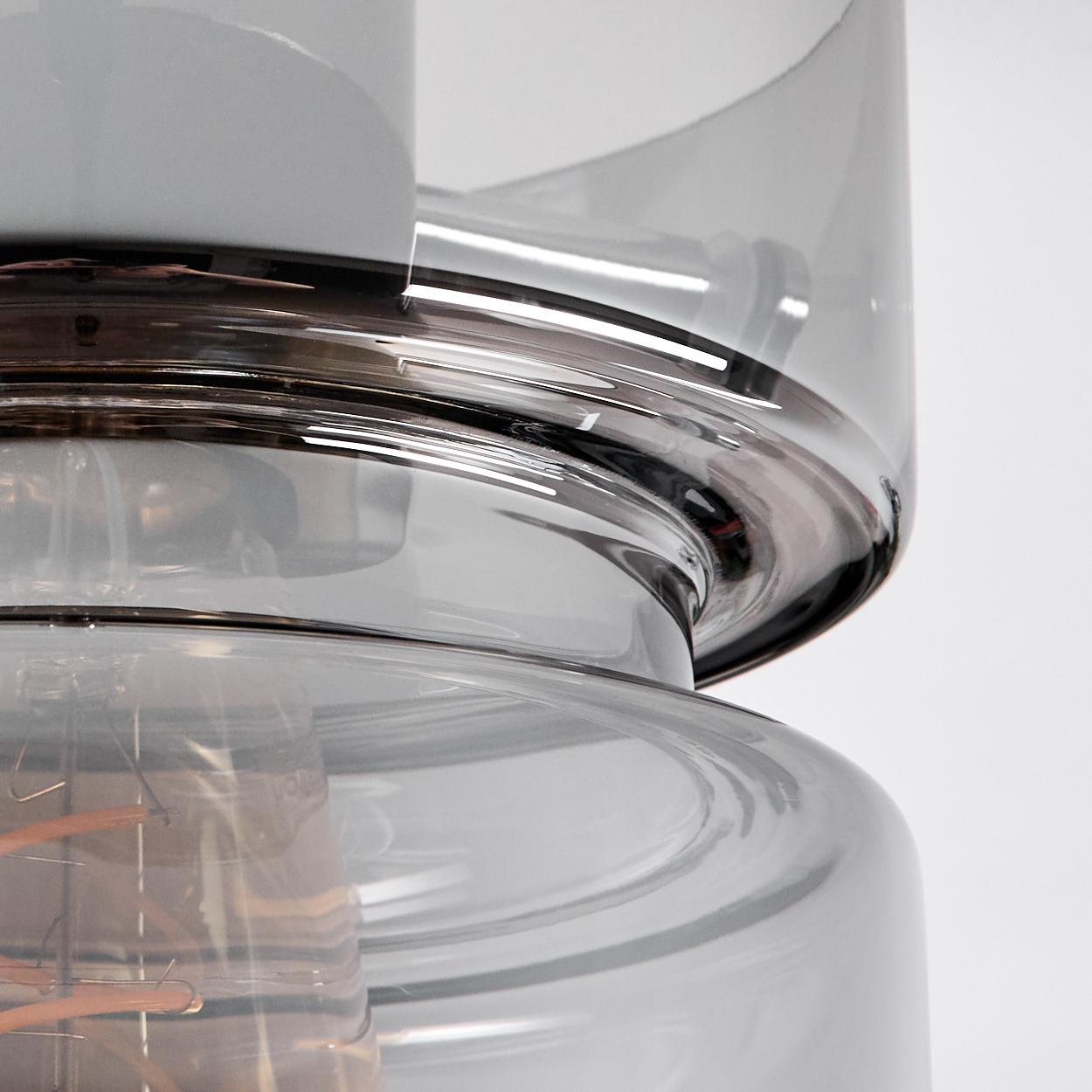Nahaufnahme einer Glasleuchte. Sie besteht aus geschichtetem, grau getöntem Glas. Im Inneren ist eine Glühbirne mit Kupferdrähten zu sehen.