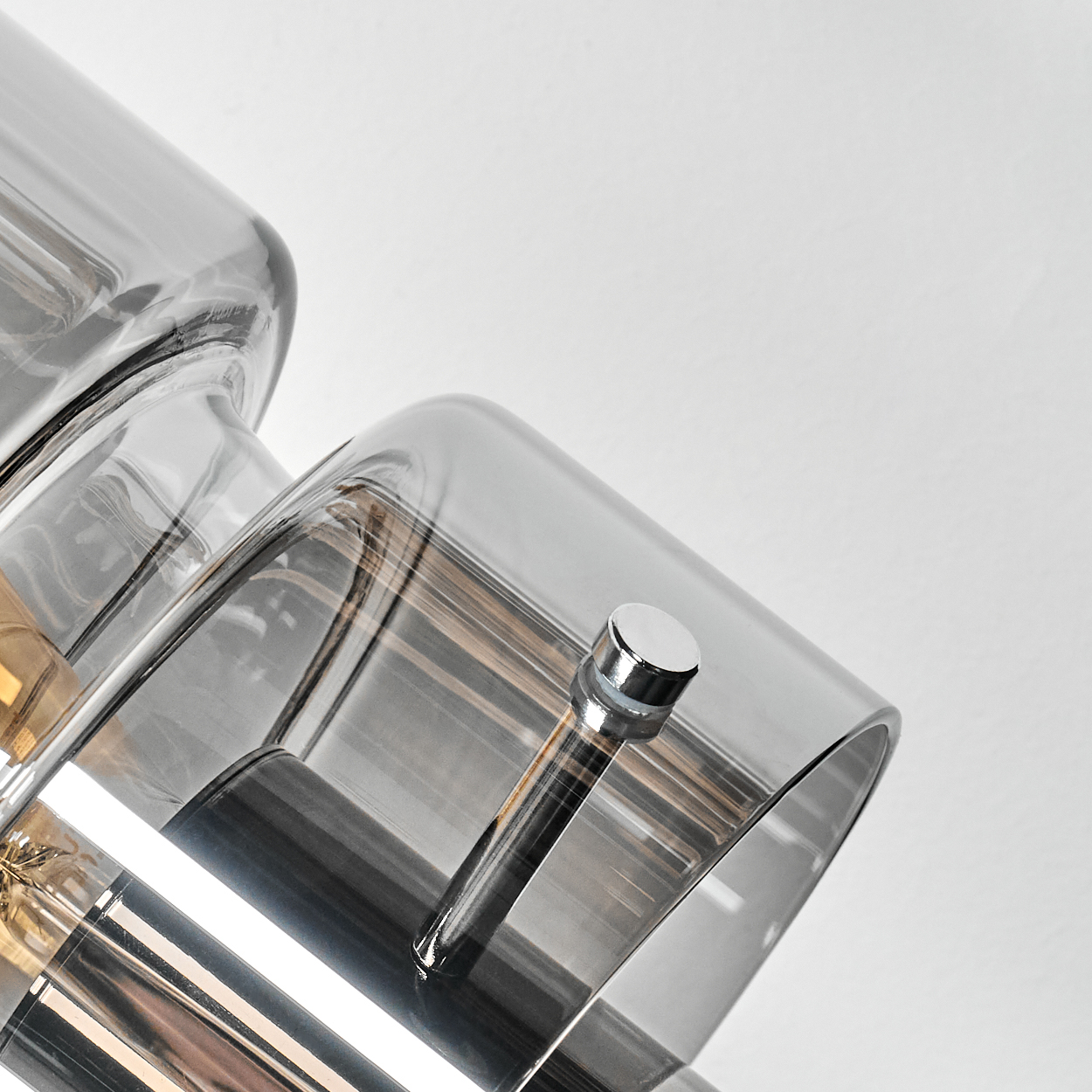 Nahaufnahme einer modernen Lampe mit grauen Glasschirmen und Chromakzenten vor weißem Hintergrund.