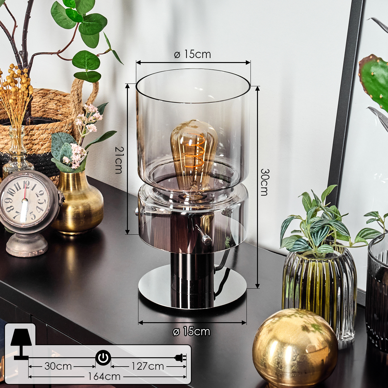 Eine moderne Lampe mit Glasschirm und sichtbarer Glühbirne. Sie steht auf einer dunklen Oberfläche mit Dekoration.