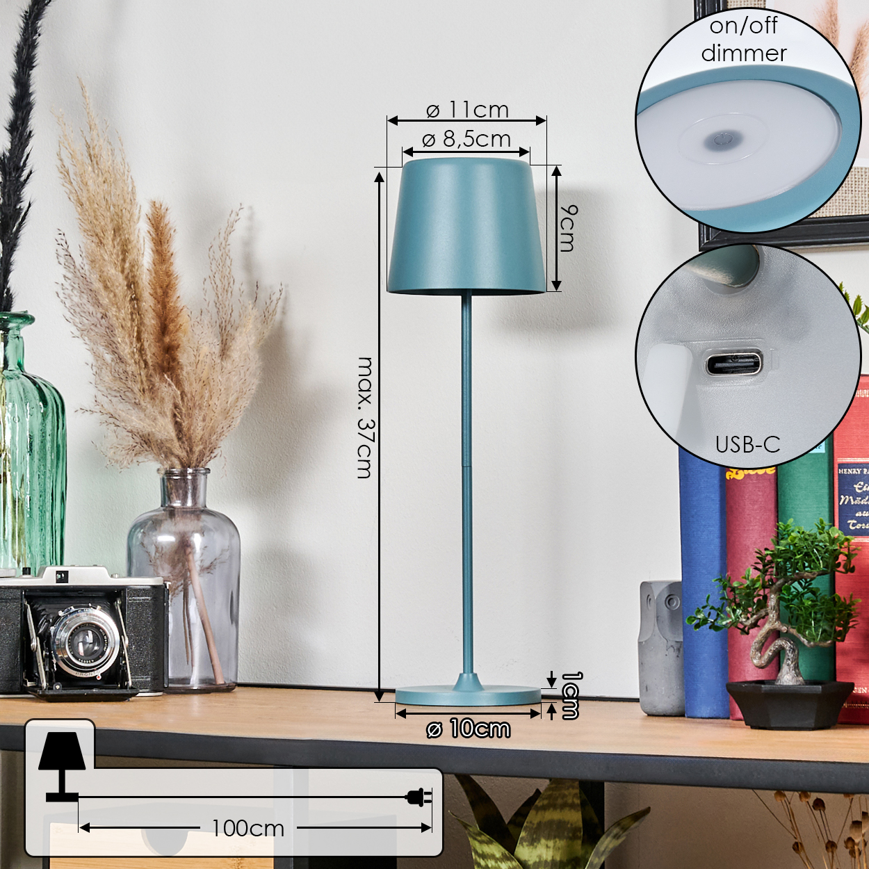 Eine teal Tischlampe mit Maßen. Sie hat einen USB-C-Anschluss, einen Dimmer und steht auf einem Holzregal mit Büchern, Pflanzen und einer Kamera.