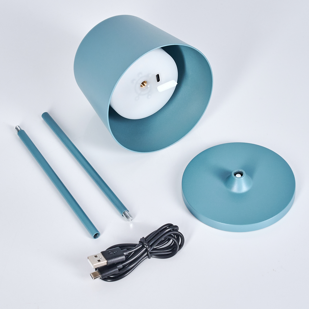 Eine zerlegte blaue Lampe mit zylindrischem Schirm, zwei Stäben, einem Sockel und einem USB-Kabel sind auf weißem Untergrund angeordnet.