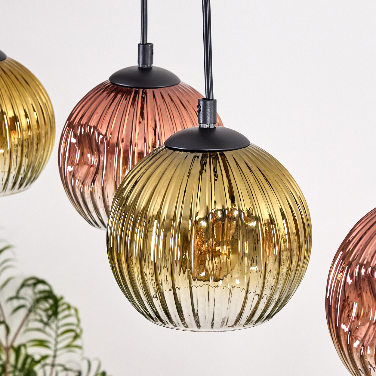 Vier kugelförmige Pendelleuchten in Gold und Kupfer. Die Leuchten haben eine gerippte Textur und hängen an schwarzen Kabeln.