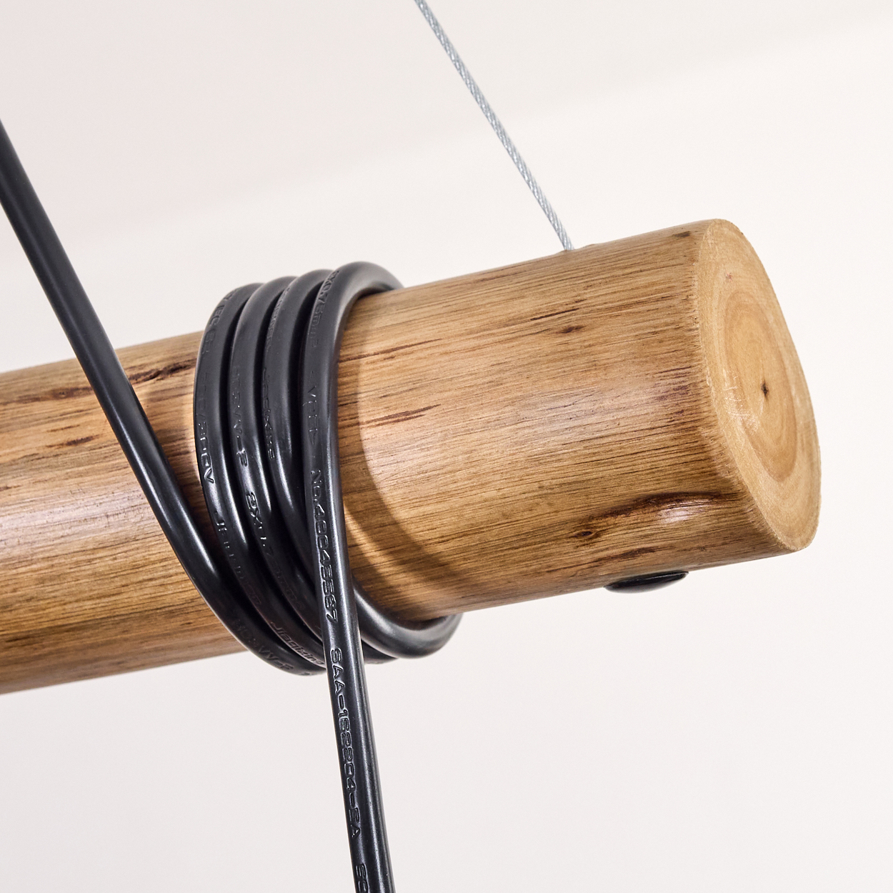 Ein Holzbalken mit einem schwarzen Elektrokabel, das darum gewickelt ist. Ein silberner Draht ist am Balken befestigt. Weißer Hintergrund.