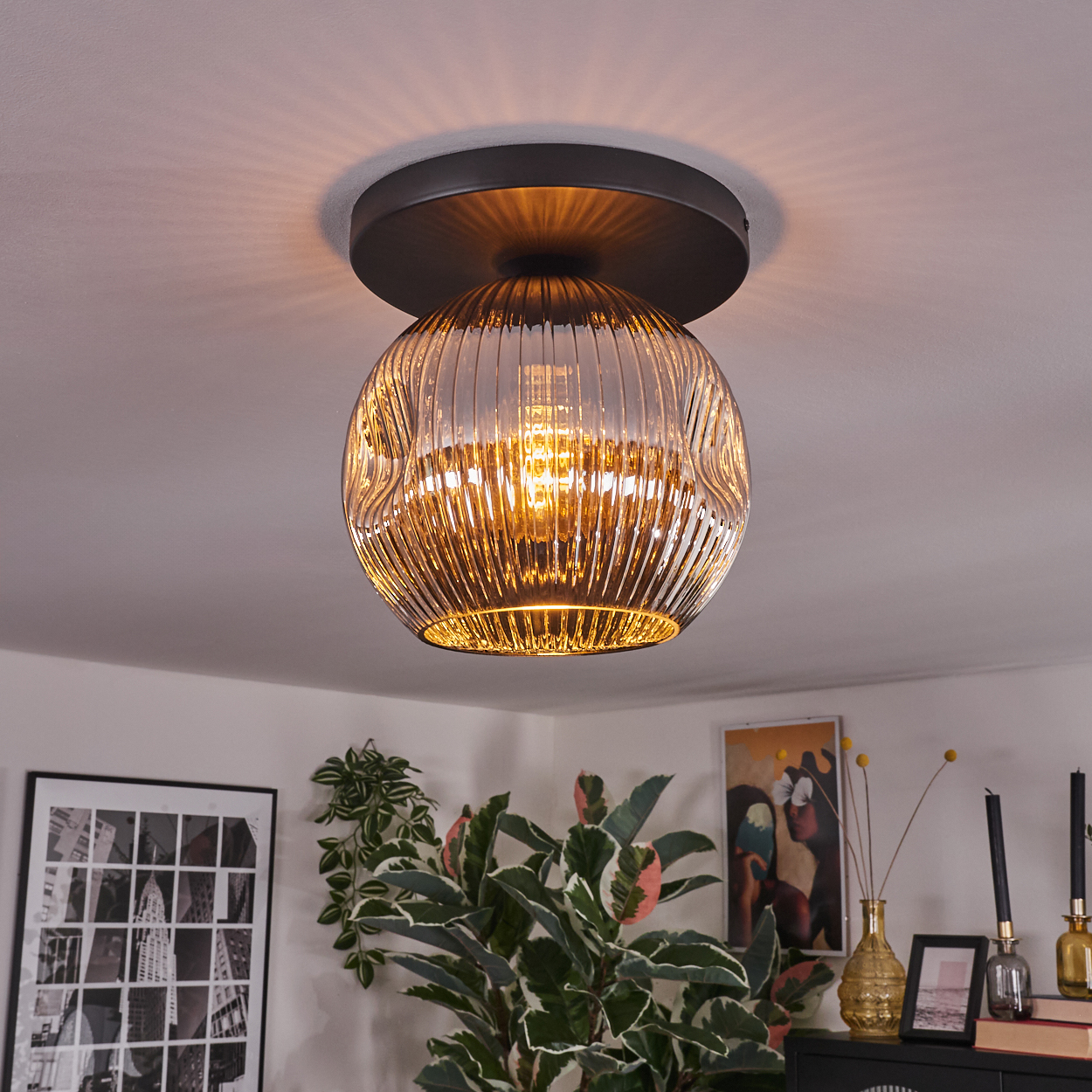 Eine dekorative Deckenlampe mit Glaskugel. Der Raum hat Pflanzen, Kunst und einen schwarzen Schrank. Das Licht scheint.