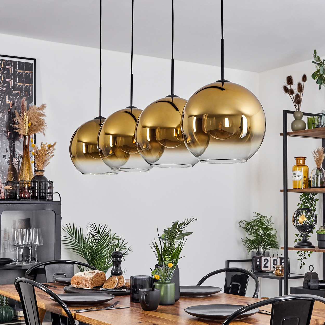 Esszimmer mit Holztisch, schwarzen Stühlen und goldenen Lampen. Geschirr, Pflanzen und Dekorationen auf dem Tisch und in Regalen.