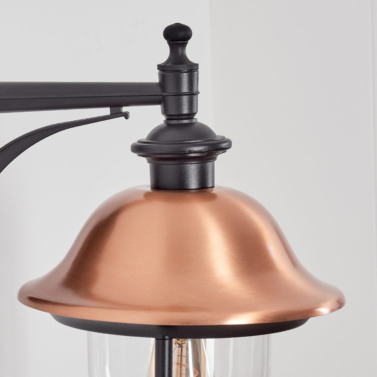 Nahaufnahme eines kupferfarbenen Lampenschirms mit schwarzem Metallrahmen. Der Hintergrund ist eine schlichte weiße Wand.
