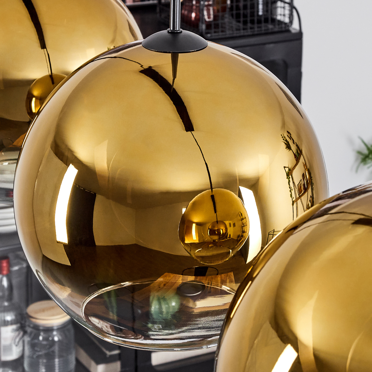 Nahaufnahme von goldenen, kugelförmigen Pendelleuchten, die Objekte im Raum reflektieren. Einige Lichter hängen von der Decke.