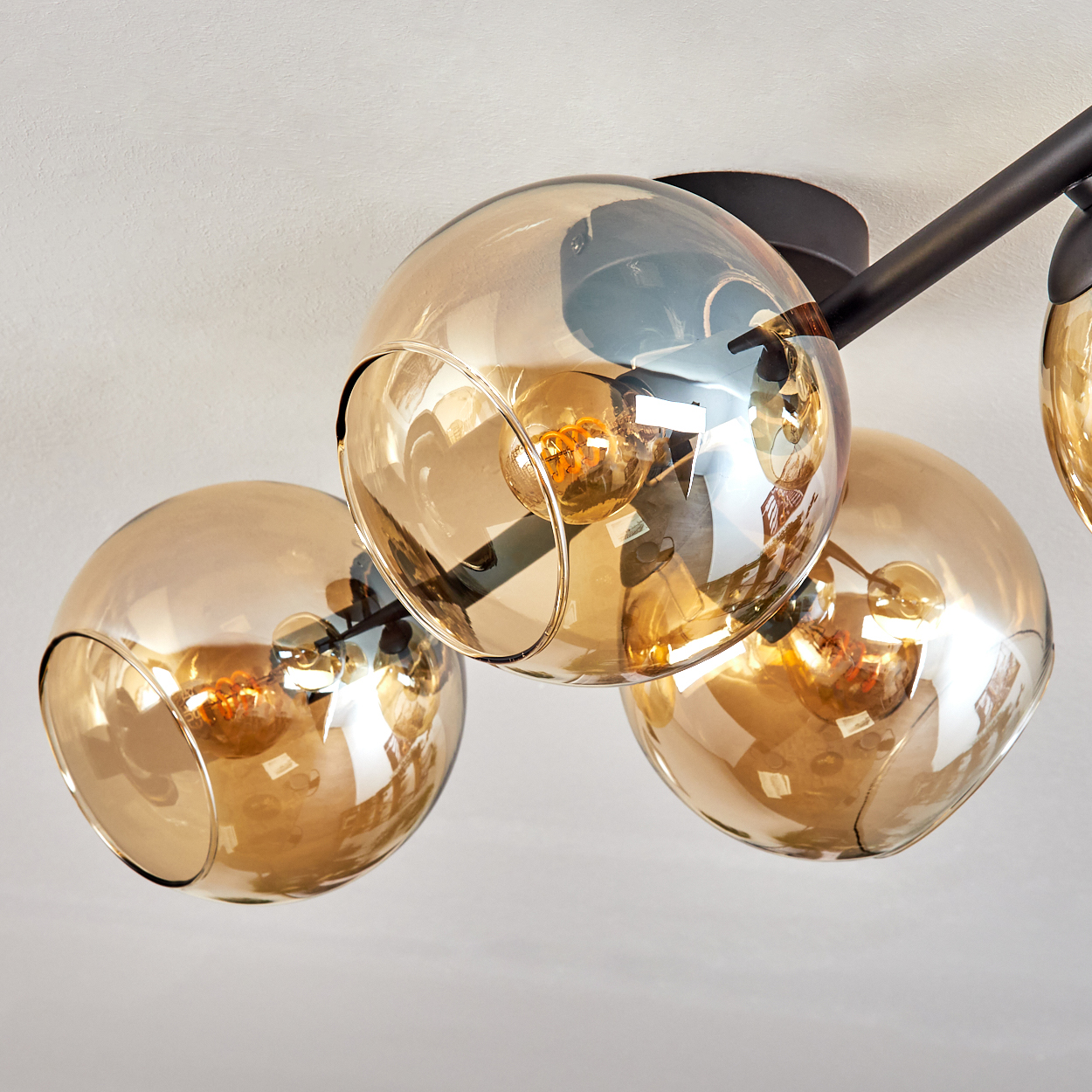 Eine moderne Deckenleuchte mit vier bernsteinfarbenen Glaskugeln, jede mit einer sichtbaren Glühbirne. Sie sind an schwarzen Metallarmen befestigt.