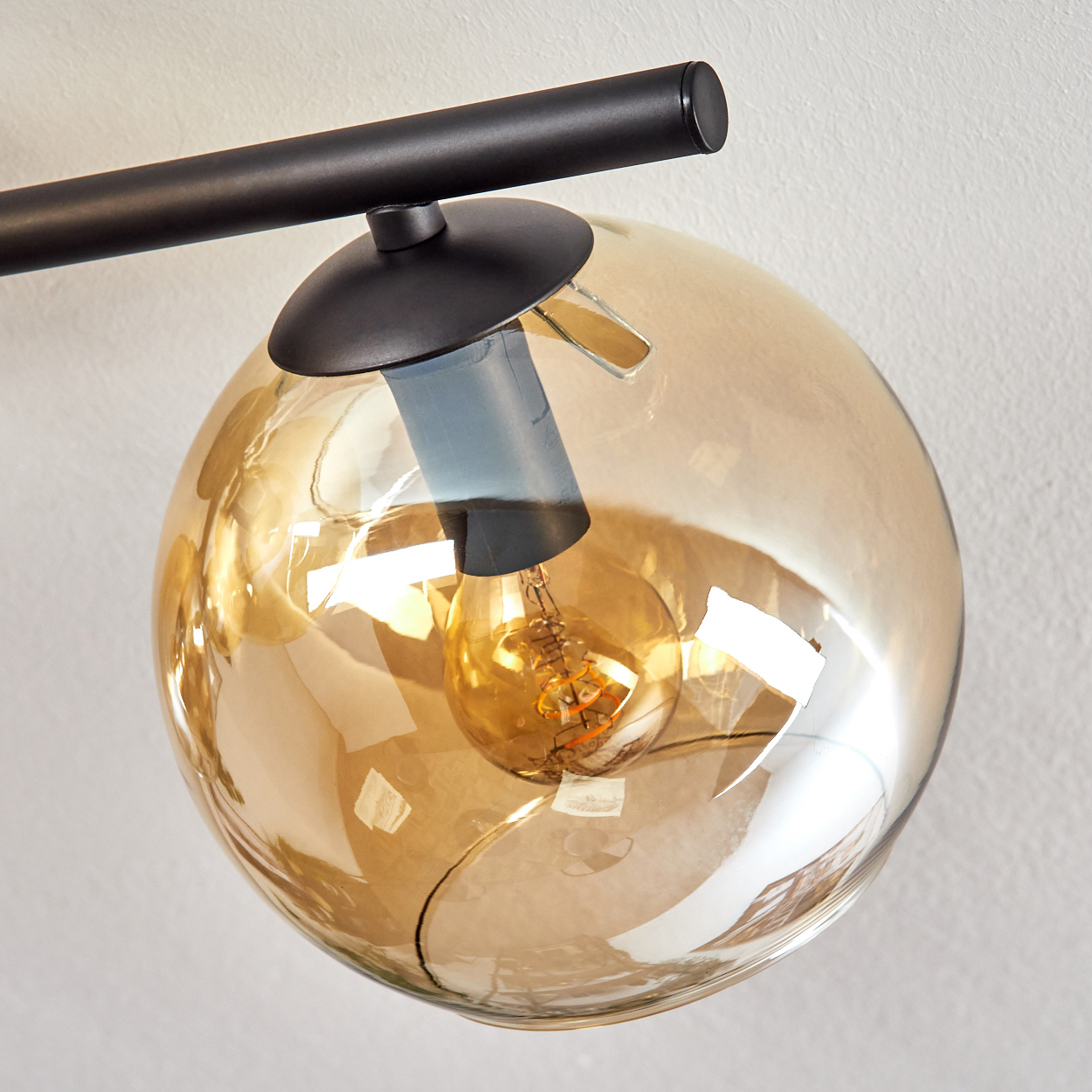 Nahaufnahme einer modernen Leuchte. Sie hat einen schwarzen Arm mit einem kugelförmigen, bernsteinfarbenen Glasschirm, der eine warme Glühbirne beherbergt.