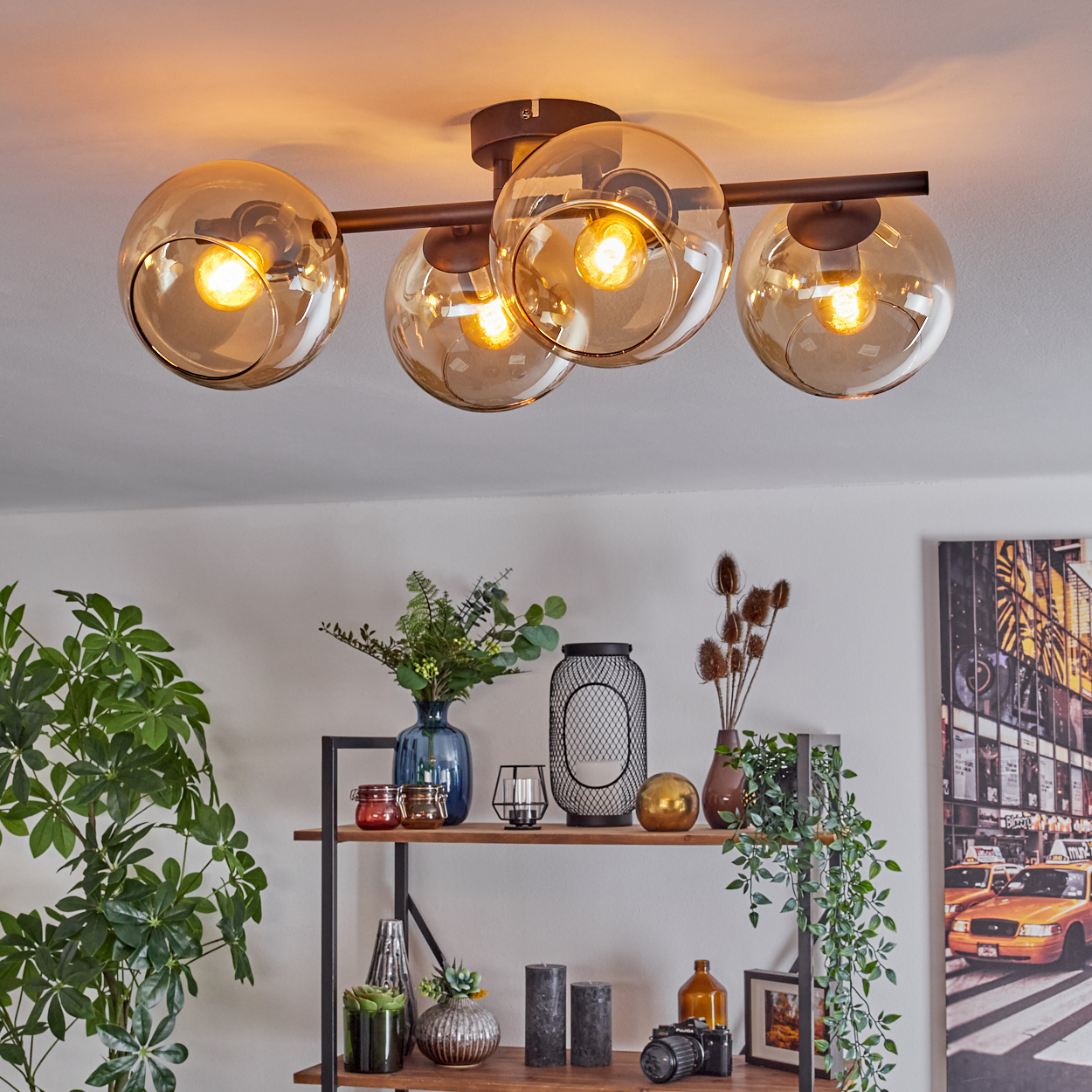 Moderne Deckenleuchte mit vier Glaskugeln. Darunter ein Regal mit Vasen, Pflanzen, Kerzen und einer Kamera. Rechts ein NYC-Stadtbild.