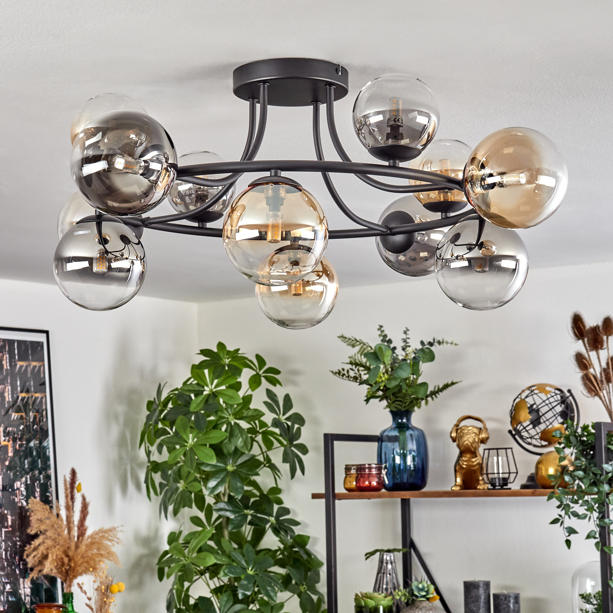 Eine moderne Deckenleuchte mit mehreren Glaskugeln hängt von der Decke. Auf Regalen stehen dekorative Gegenstände wie Pflanzen und Skulpturen.