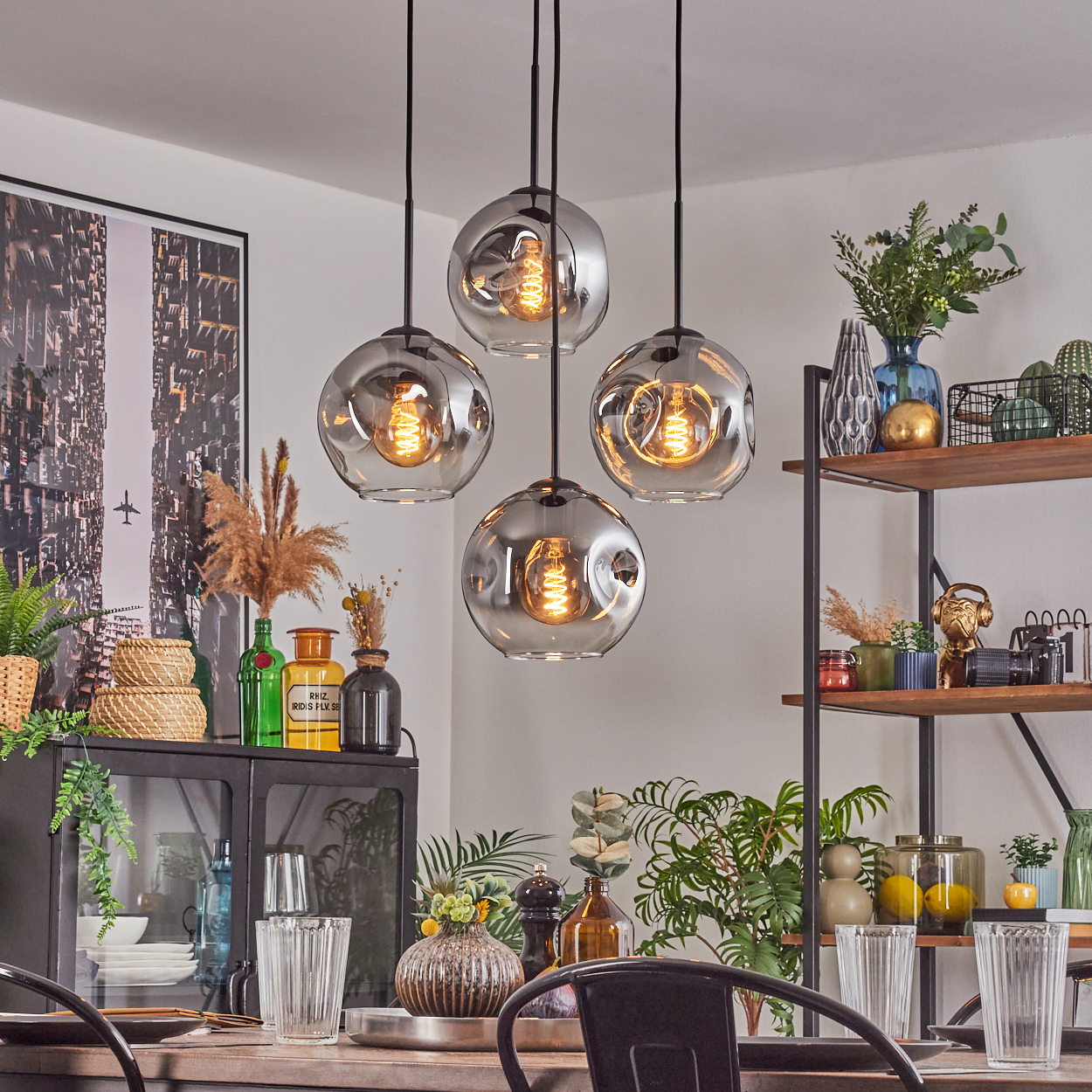 Esszimmer mit vier Kugellampen. Schwarzer Tisch mit Stühlen, Gläsern und Pflanzen. Regale mit Vasen und Dekoration.