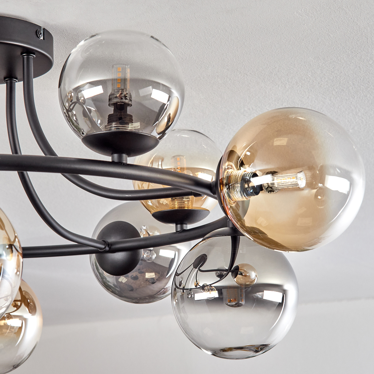 Eine moderne Deckenleuchte mit mehreren Glaskugelschirmen und schwarzen Metallarmen vor einer weißen Decke.
