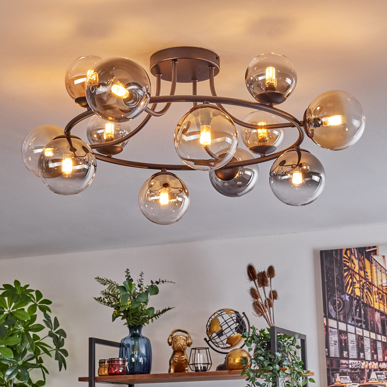 Eine moderne Deckenleuchte mit mehreren Glaskugelschirmen. Darunter ein Regal mit Dekoration: Pflanzen, eine goldene Bulldogge und ein Globus.