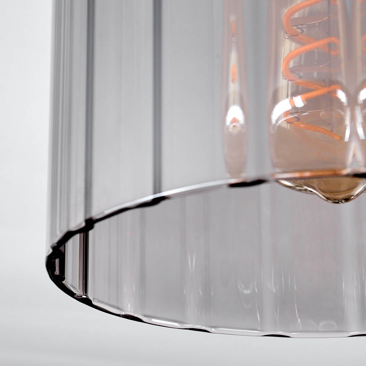 Nahaufnahme einer Glasleuchte. Das Glas ist klar mit vertikalen Linien. Ein orangefarbener Glühfaden ist innen sichtbar, mit silberner Basis.