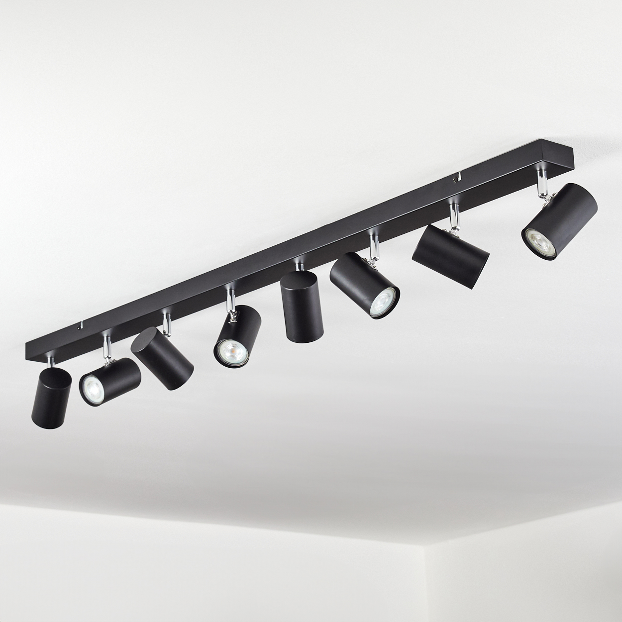 Schwarze Deckenstrahler-Leuchte mit acht verstellbaren Lichtern. Die Leuchten sind zylindrisch und zeigen in verschiedene Richtungen.