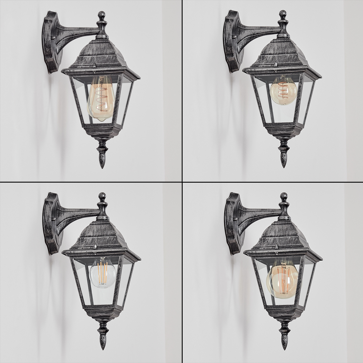 Vier graue Außenlampen mit Glasscheiben und Glühbirnen an einer weißen Wand. Jede Lampe ist an einer Halterung befestigt.