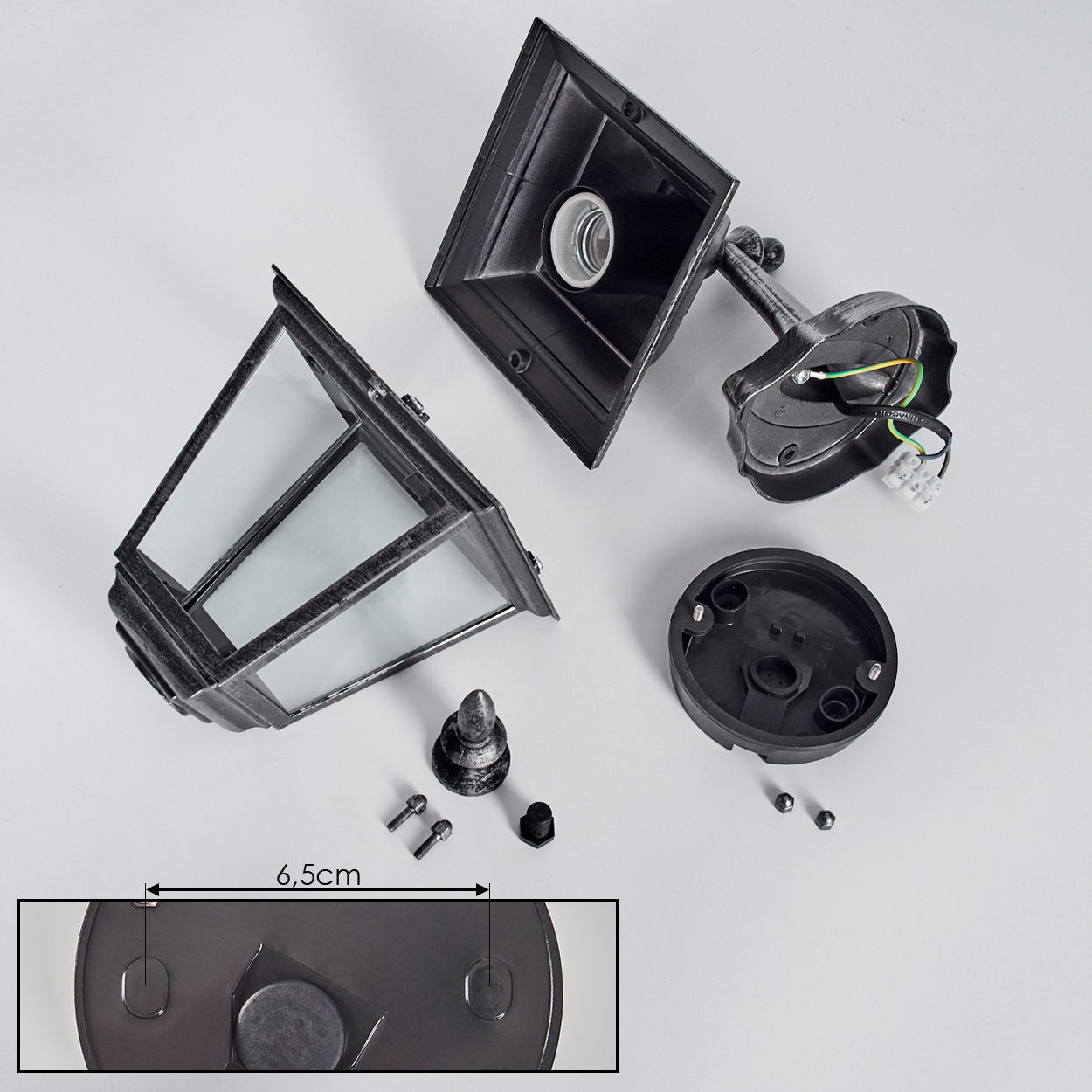 Zerlegte Außenlampe mit Glasscheiben, Schrauben und Sockel auf weißer Oberfläche. Die Lampe ist schwarz mit silbernen Akzenten.