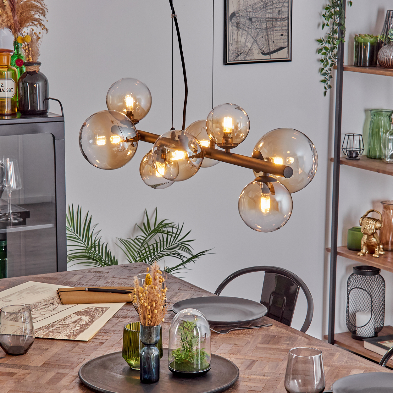 Ein Esszimmer mit Holztisch, modernem Kronleuchter mit Kugellampen und diversen Dekorationsartikeln.