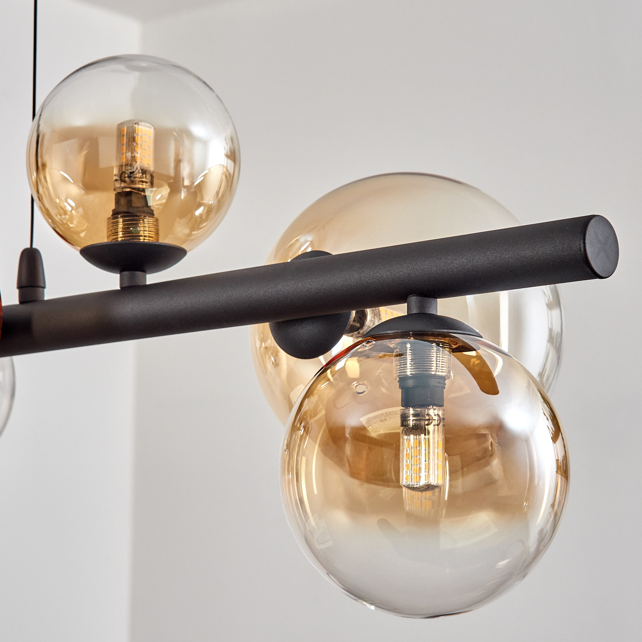 Eine moderne Deckenleuchte mit kugelförmigen Glasschirmen in Bernsteinfarbe mit freiliegenden LED-Lampen. Die Leuchte ist schwarz, mit weißer Wand im Hintergrund.