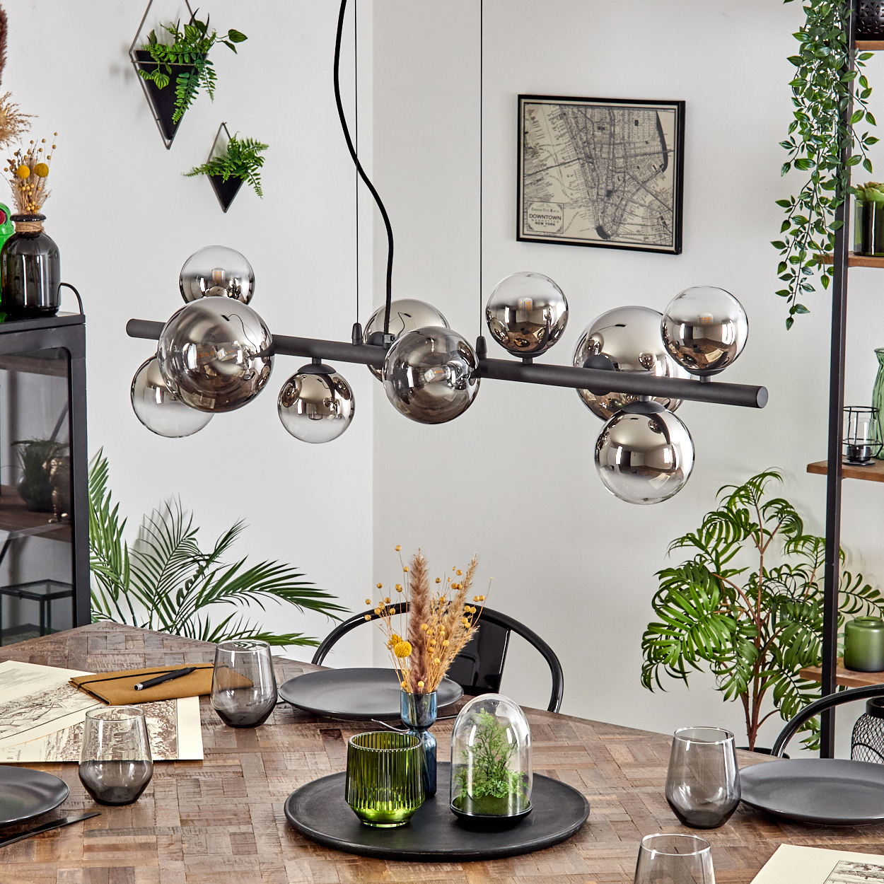 Ein Esszimmer mit einem Holztisch, der mit Tellern, Gläsern und einem Mittelstück gedeckt ist. Darüber hängt ein moderner Kronleuchter mit kugelförmigen Lichtern.