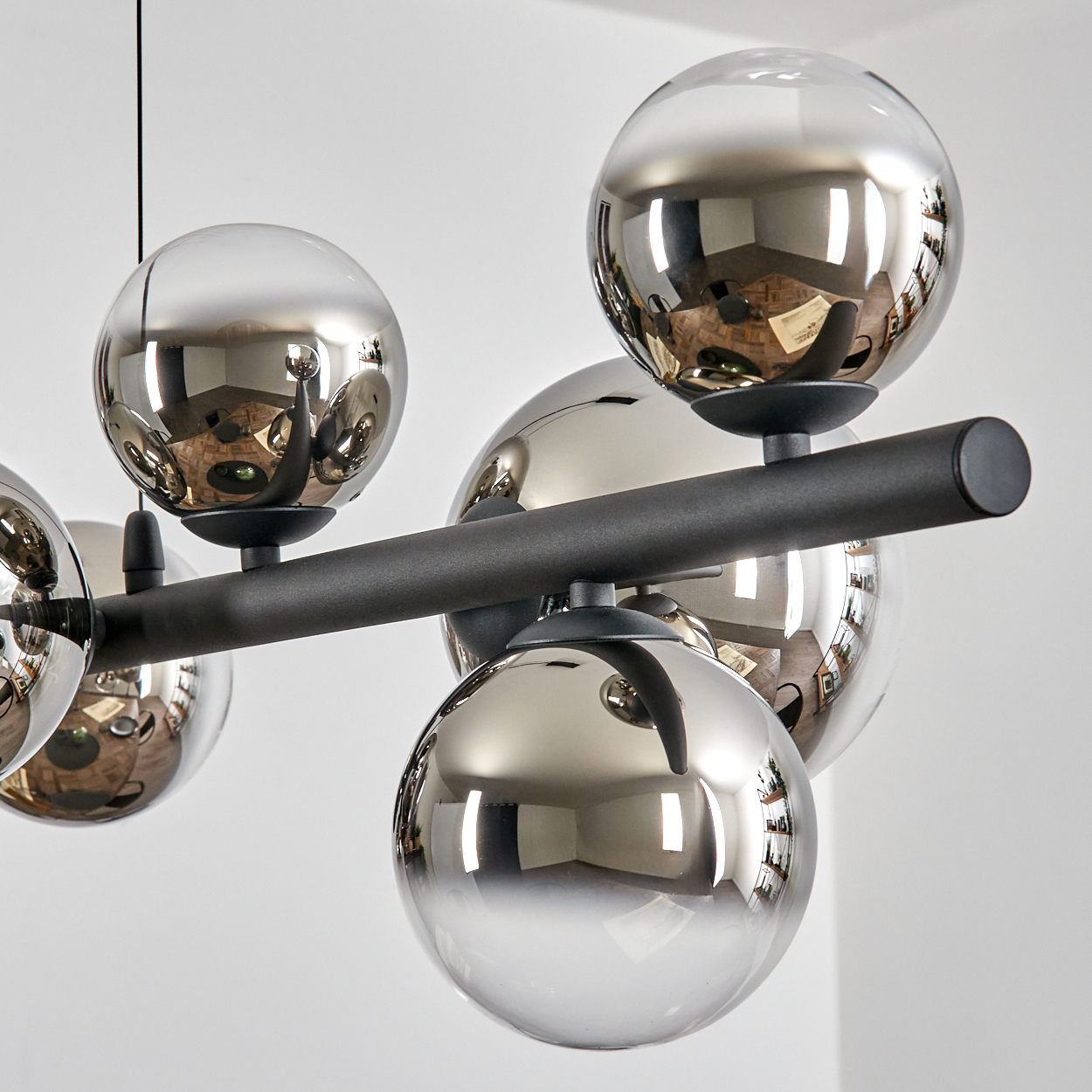 Eine moderne Deckenleuchte mit mehreren reflektierenden Chromkugeln, die an einem schwarzen Metallrahmen befestigt sind, der den Raum reflektiert.