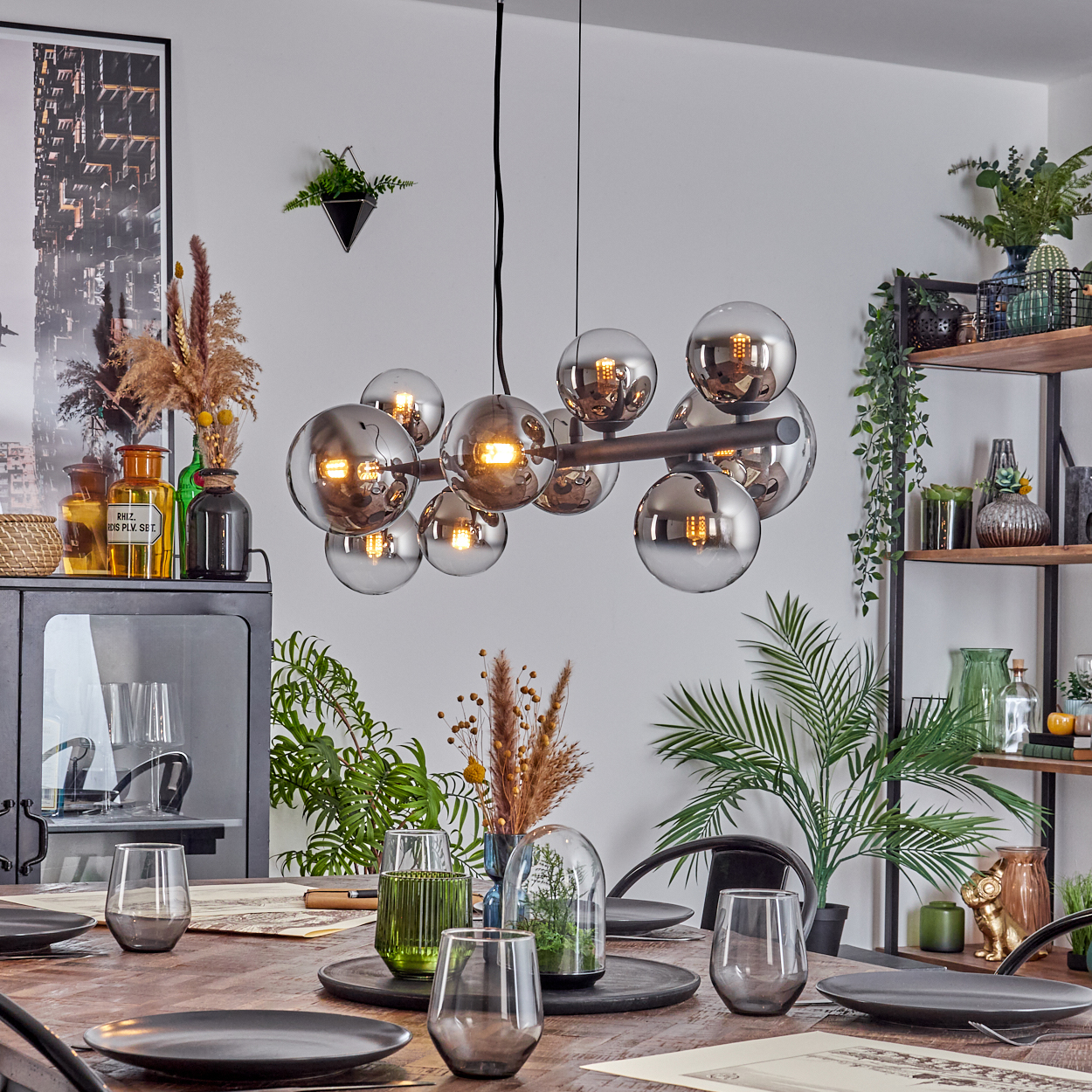 Ein Esszimmer mit Holztisch, modernem Kronleuchter und dekorativen Pflanzen. Gläser und Teller sind für eine Mahlzeit auf dem Tisch gedeckt.