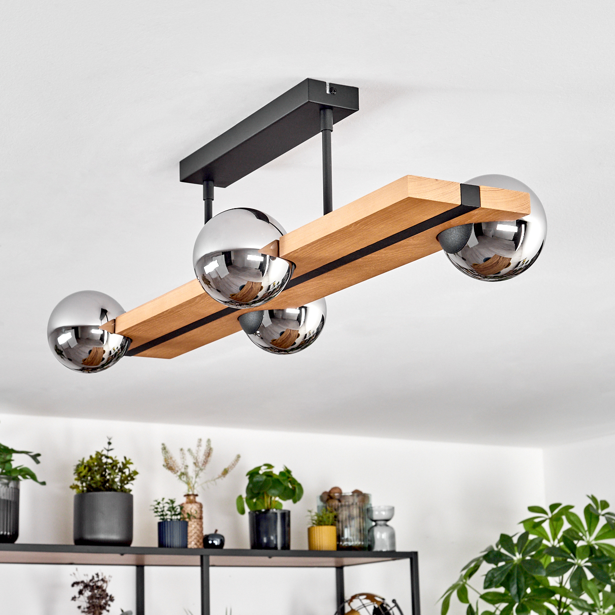 Eine moderne Deckenlampe mit vier Chromkugeln. Sie hängt von einem schwarzen Rahmen über einem Regal mit Pflanzen und Deko.