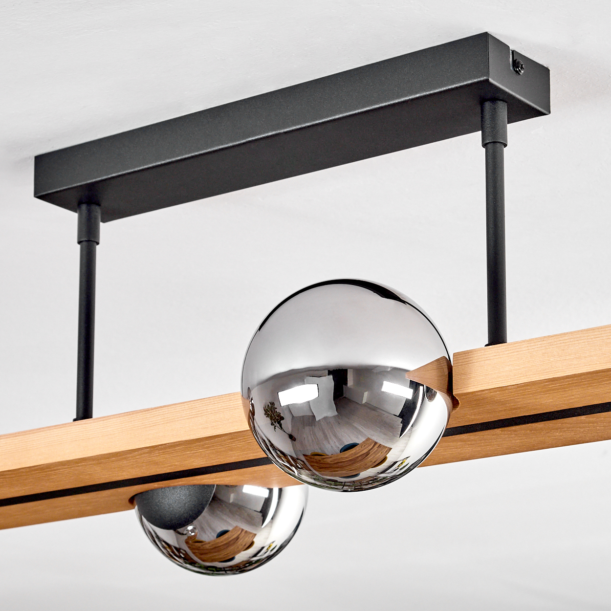 Eine moderne Deckenlampe mit zwei reflektierenden Chromkugeln, die unter einem Holzbalken hängen. Ein schwarzer Metallrahmen trägt die Lampe.