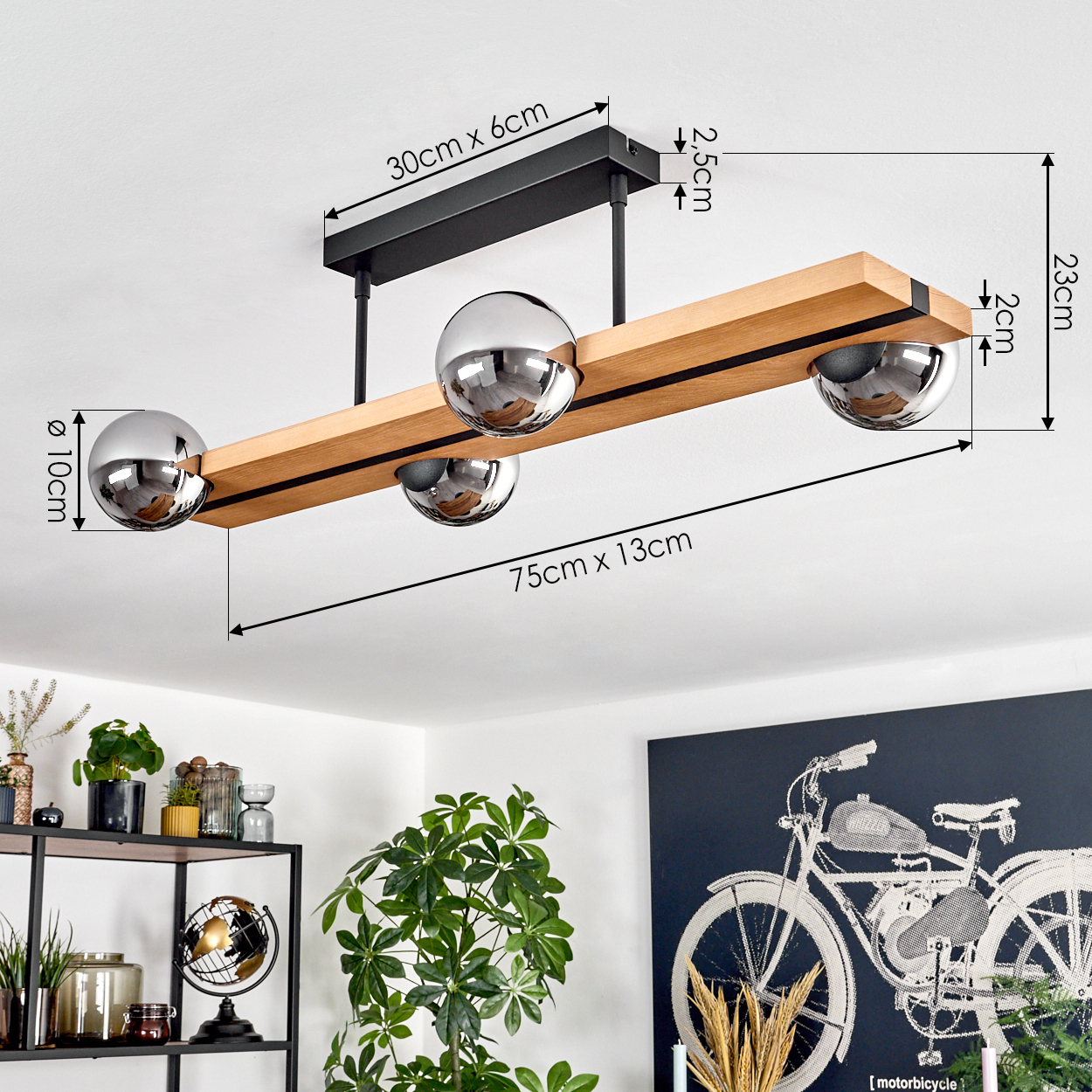 Eine moderne Holz- und Metall-Deckenleuchte mit vier kugelförmigen Lichtern. Im Hintergrund Pflanzen, Regale und ein Fahrradkunstwerk.