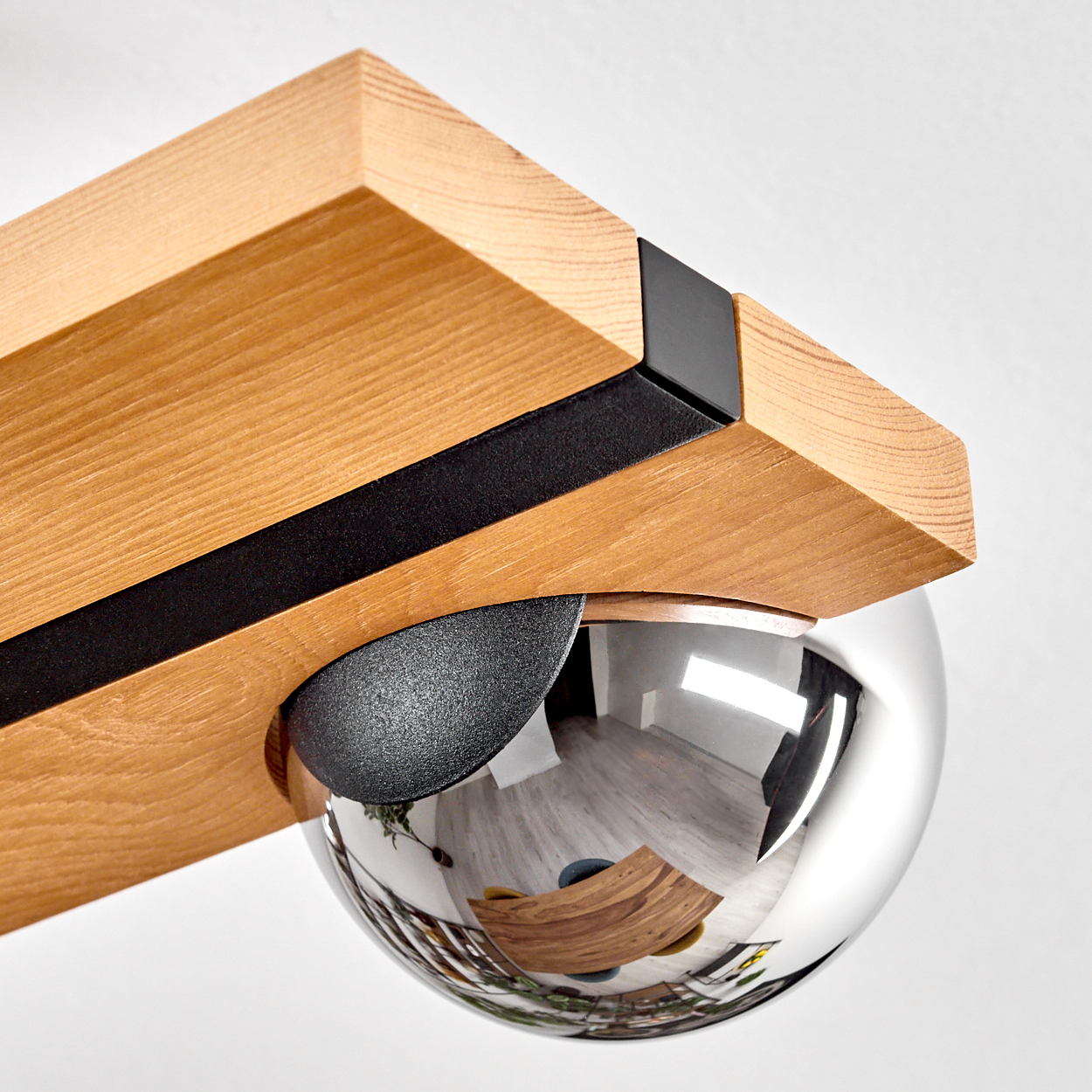 Nahaufnahme eines Holzbalkens mit schwarzen Akzenten und einer reflektierenden Chromkugel. Die Kugel spiegelt einen Raum mit einem Holztisch wider.